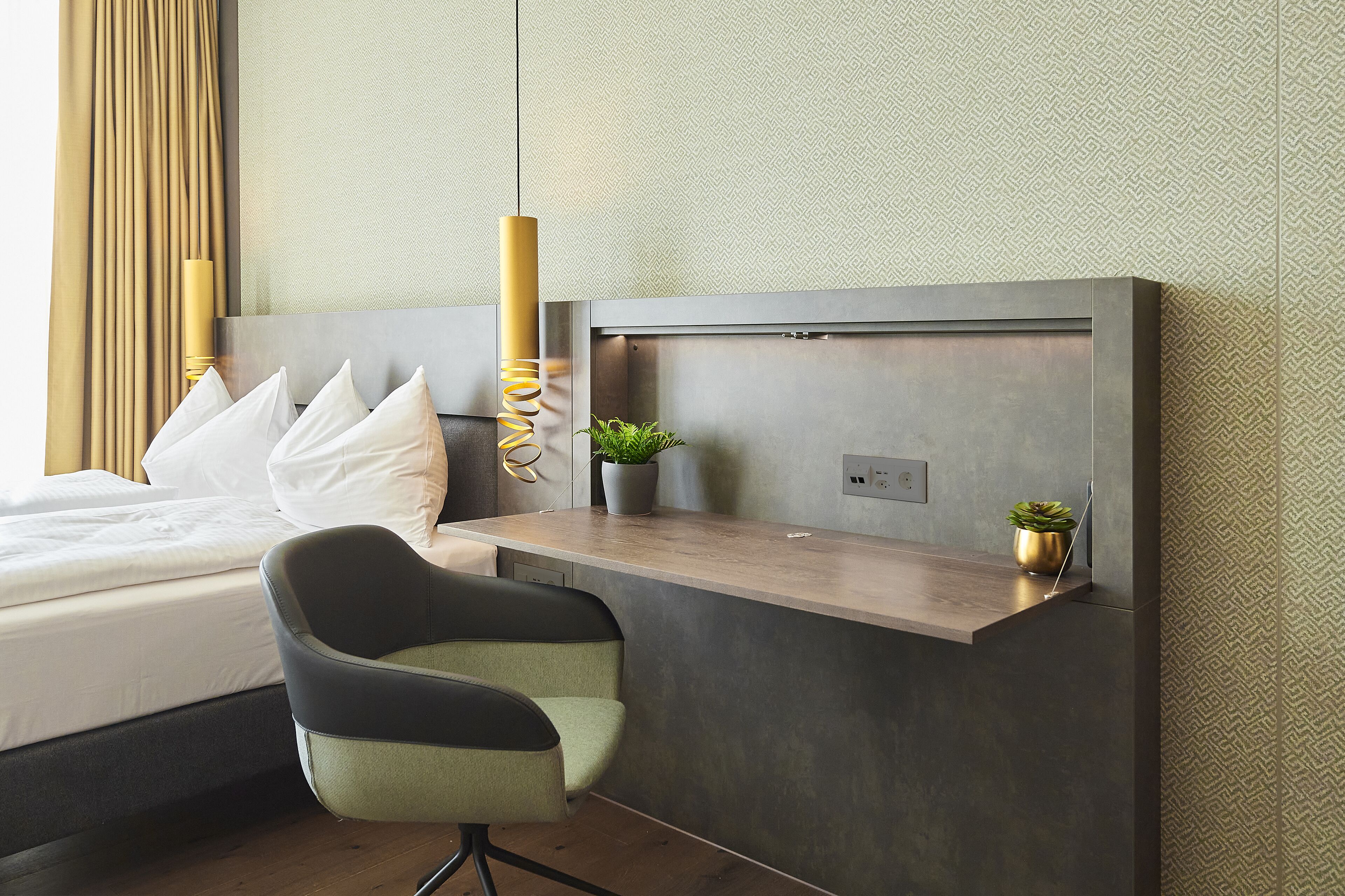 Une chambre d’hôtel moderne, équipée d’un lit, d’un bureau et de deux plantes en pot.