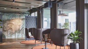 A modern lobby with leather seating, a large wall mural, and a potted plant. - Lumen Apartments (Schenkon)