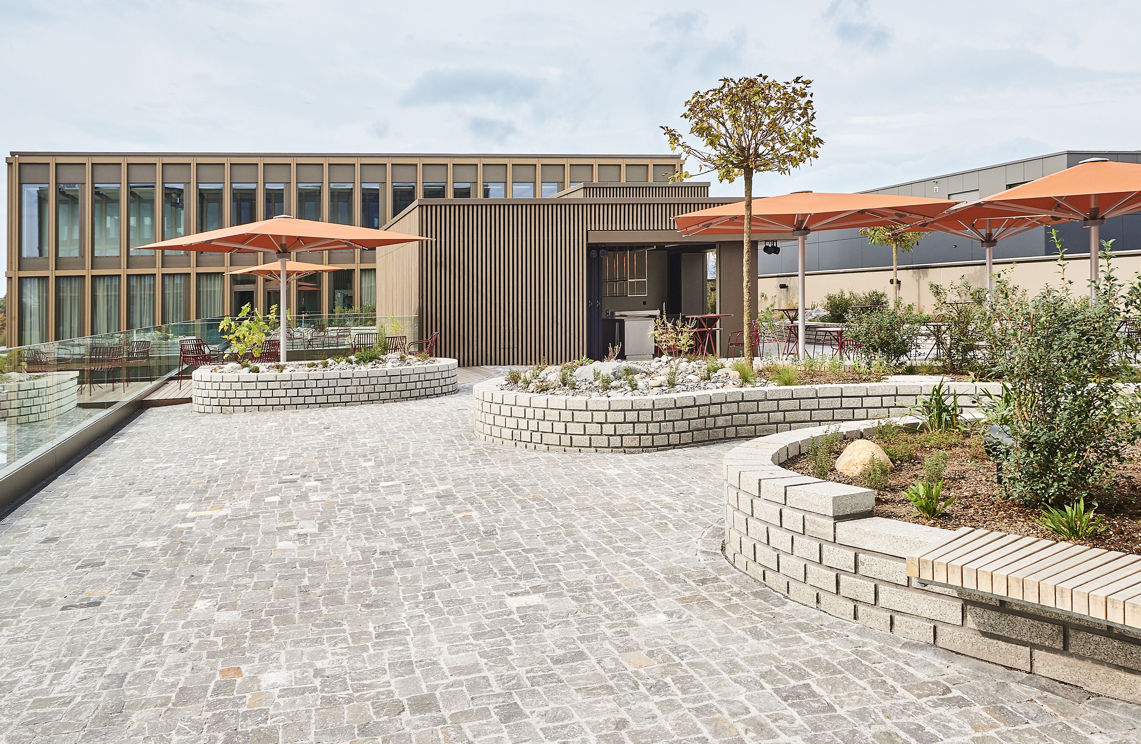Eine moderne Außenpatio mit Steinboden, Sitzbereichen und orangefarbenen Sonnenschirmen.