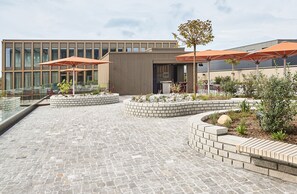 A modern outdoor patio with stone flooring, seating areas, and orange umbrellas. - Lumen Apartments (Schenkon)