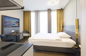 A hotel room with a bed, a desk, a chair, a TV, and a plant. - Lumen Apartments (Schenkon)