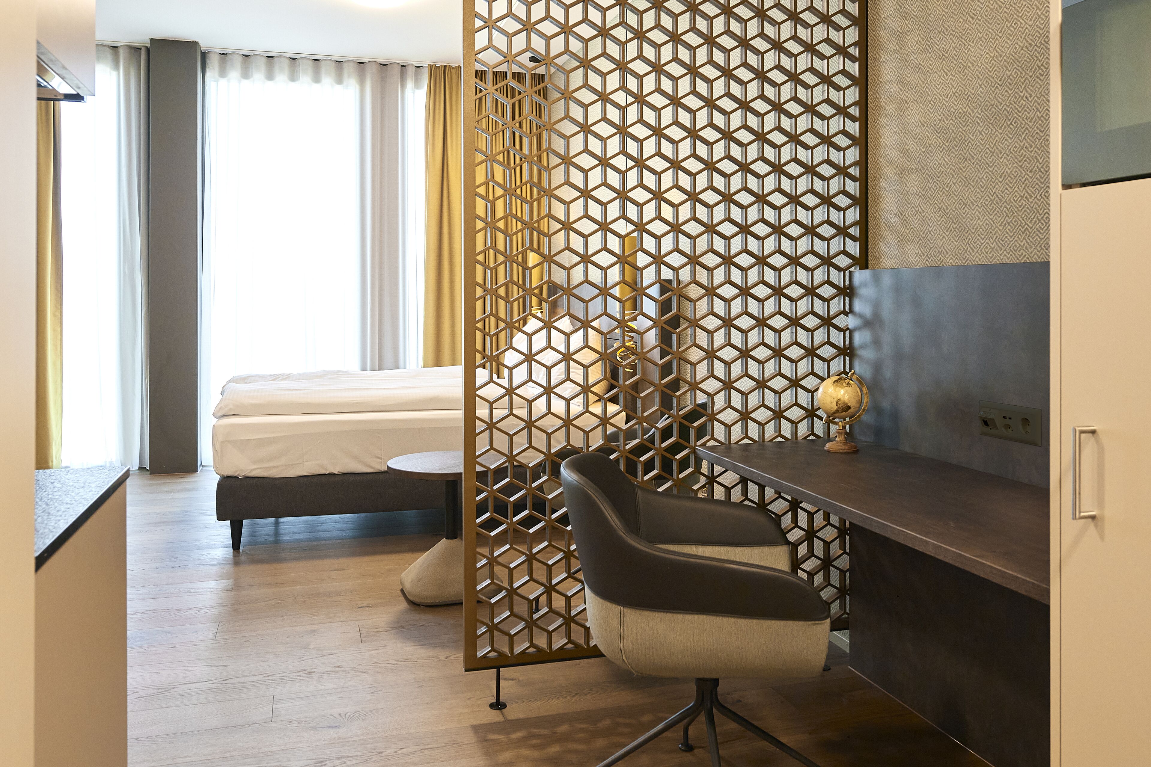 A hotel room with a bed, a desk with a chair, a decorative screen, and a globe on the desk.