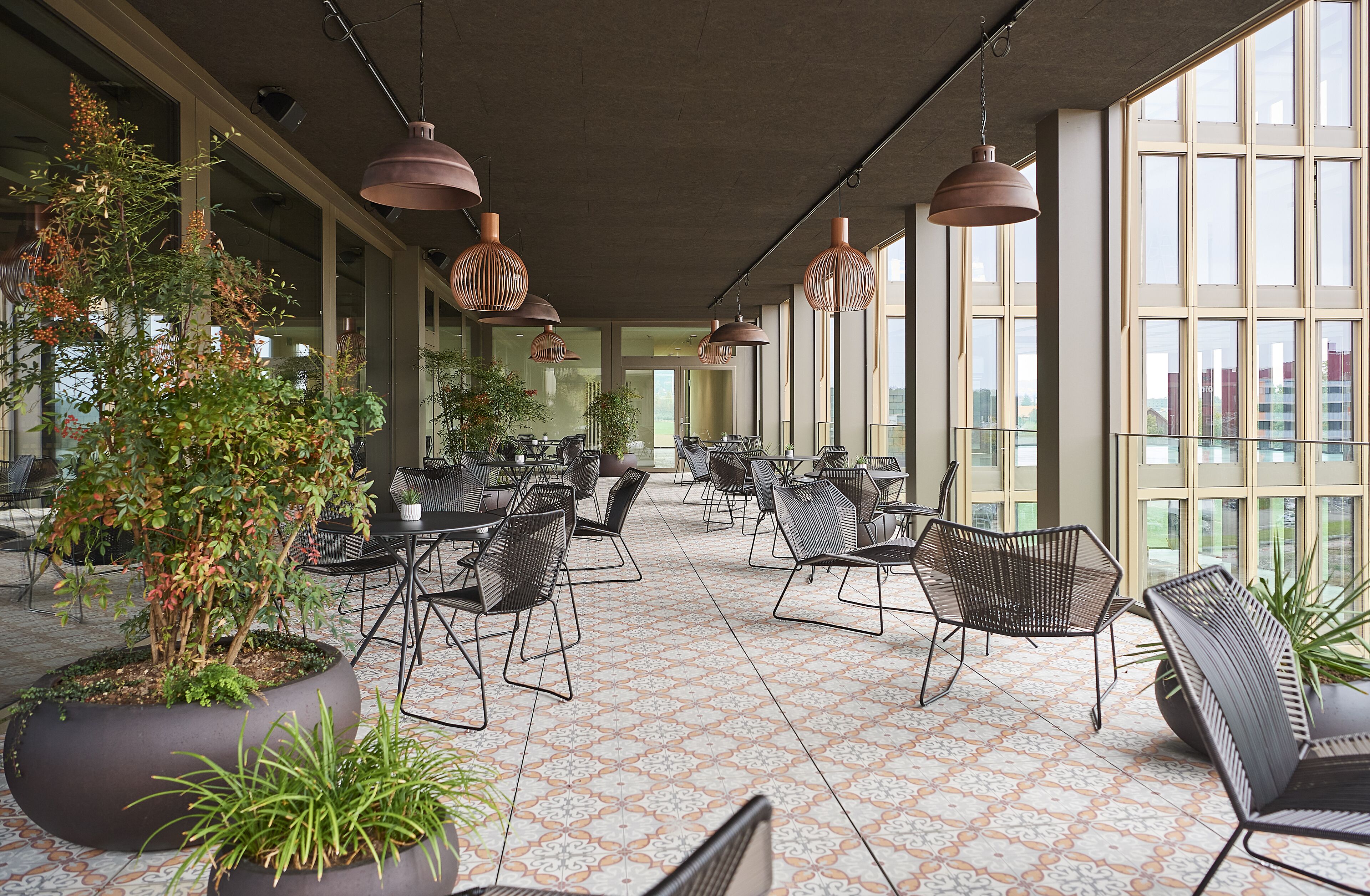 A spacious indoor area with large windows, modern furniture, and hanging pendant lights.