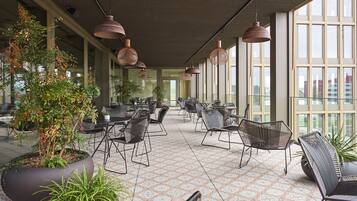 A spacious indoor area with large windows, modern furniture, and hanging pendant lights.