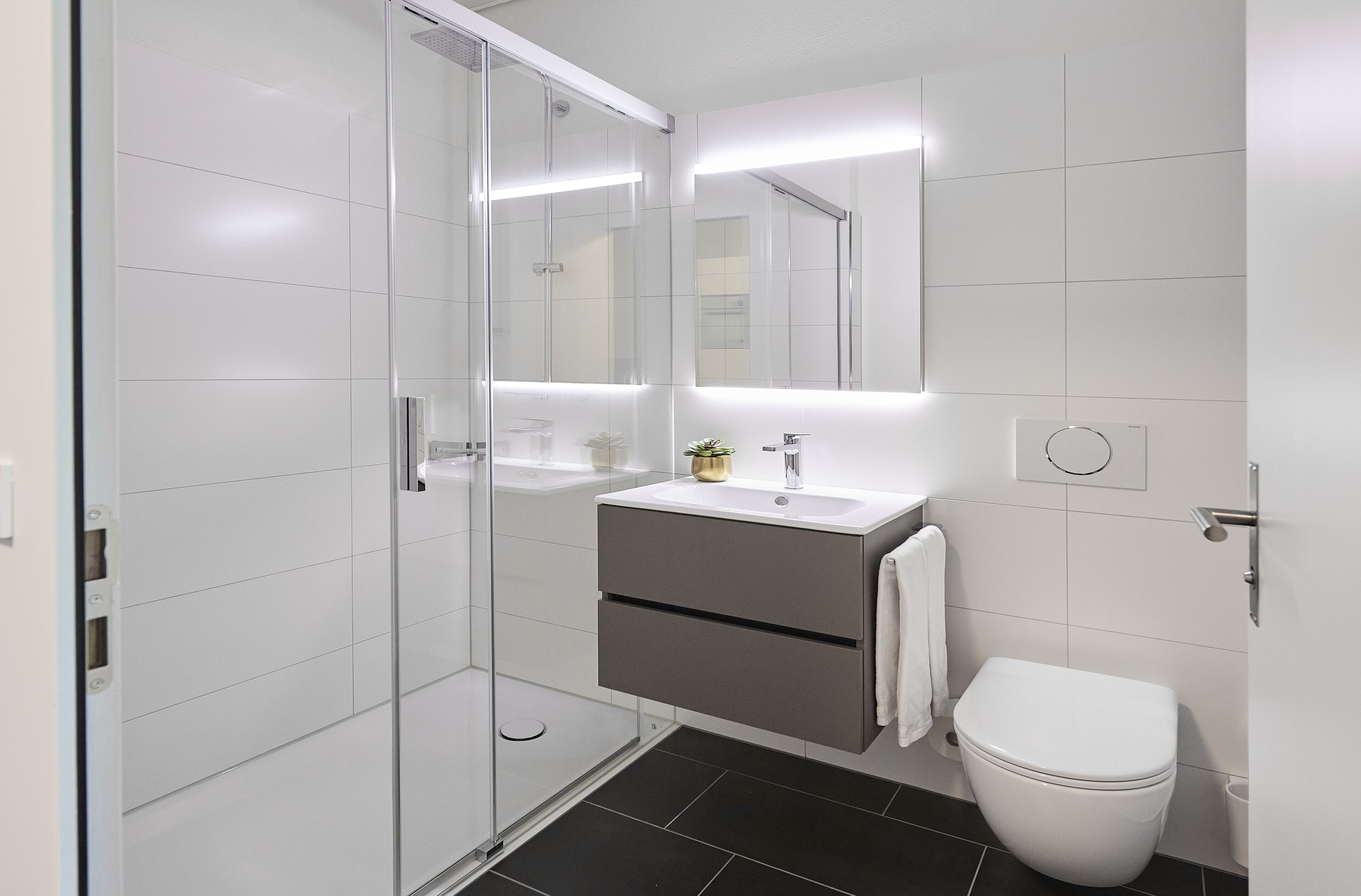 Un baño moderno con cabina de ducha de vidrio, un lavamanos blanco con detalle dorado y un inodoro blanco.