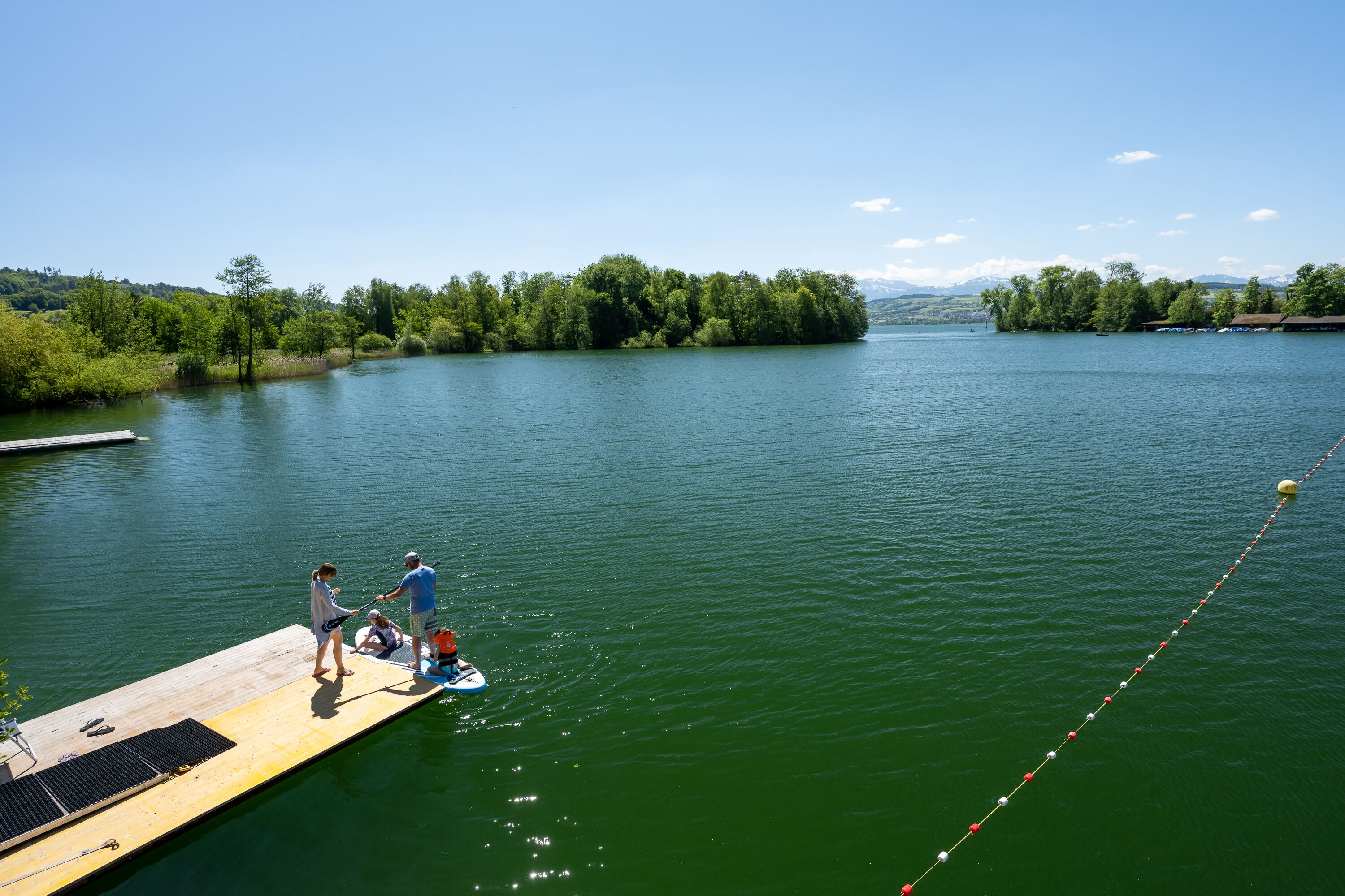 A wooden dock extending into a calm lake with a clear sky.