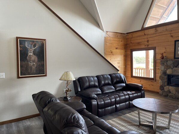 A living room with a leather sofa, a small table, a lamp, a fireplace, and a large window. - Gorgeous HERO Lodge Nestled in a 40+ acre Bio-Diverse Setting (Washington)