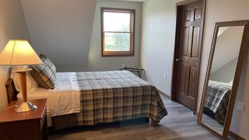 A bedroom with a bed, a nightstand, a lamp, a window, a door, and a mirror.