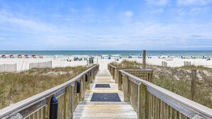 A wooden boardwalk leading to a beach with umbrellas and people. - Shoalwater 804 (Orange Beach)