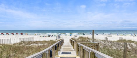 A wooden boardwalk leading to a beach with umbrellas and people.