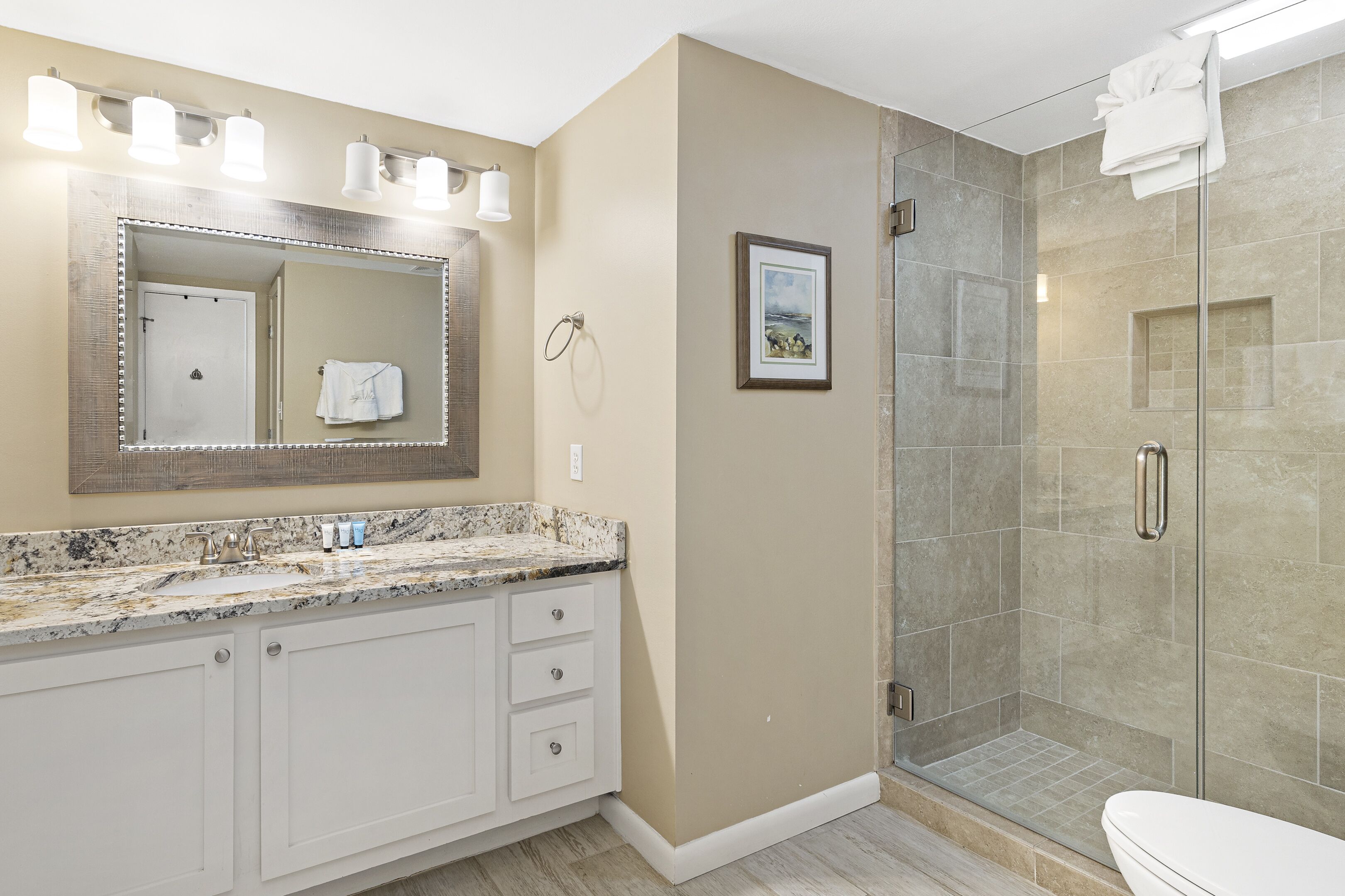 A bathroom with a marble sink, a large mirror, a framed picture on the wall, and a glass shower enclosure.