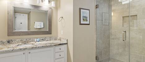 A bathroom with a marble sink, a large mirror, a framed picture on the wall, and a glass shower enclosure.