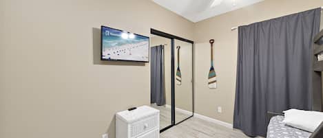 A bedroom with a bed, a television, a mirror, a ceiling fan, and a small white chest of drawers.