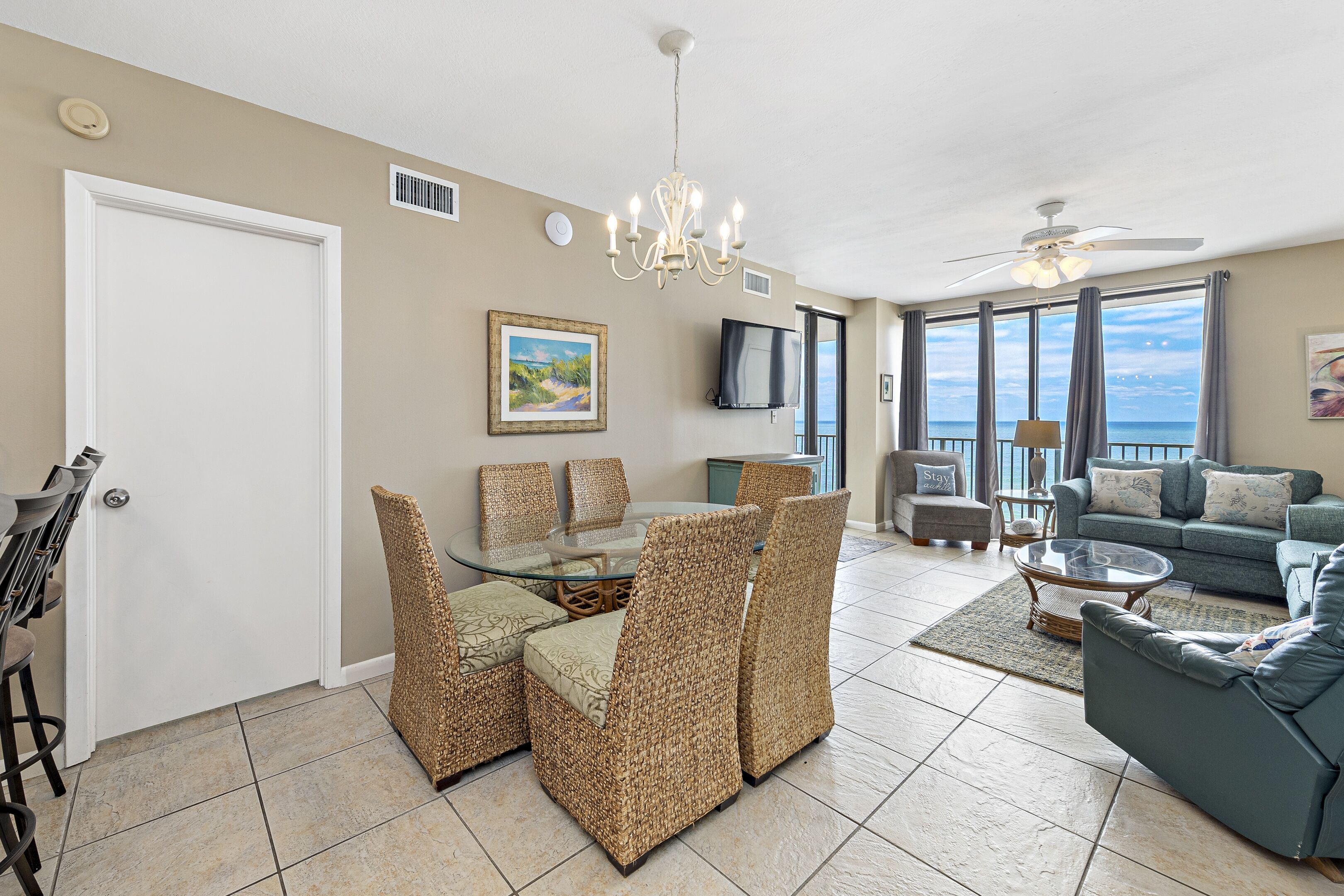A spacious living room with a glass dining table, wicker chairs, a blue sofa, and a ceiling fan.