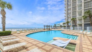 A pool area with lounge chairs, a palm tree, and a building with balconies. - Shoalwater 804 (Orange Beach)