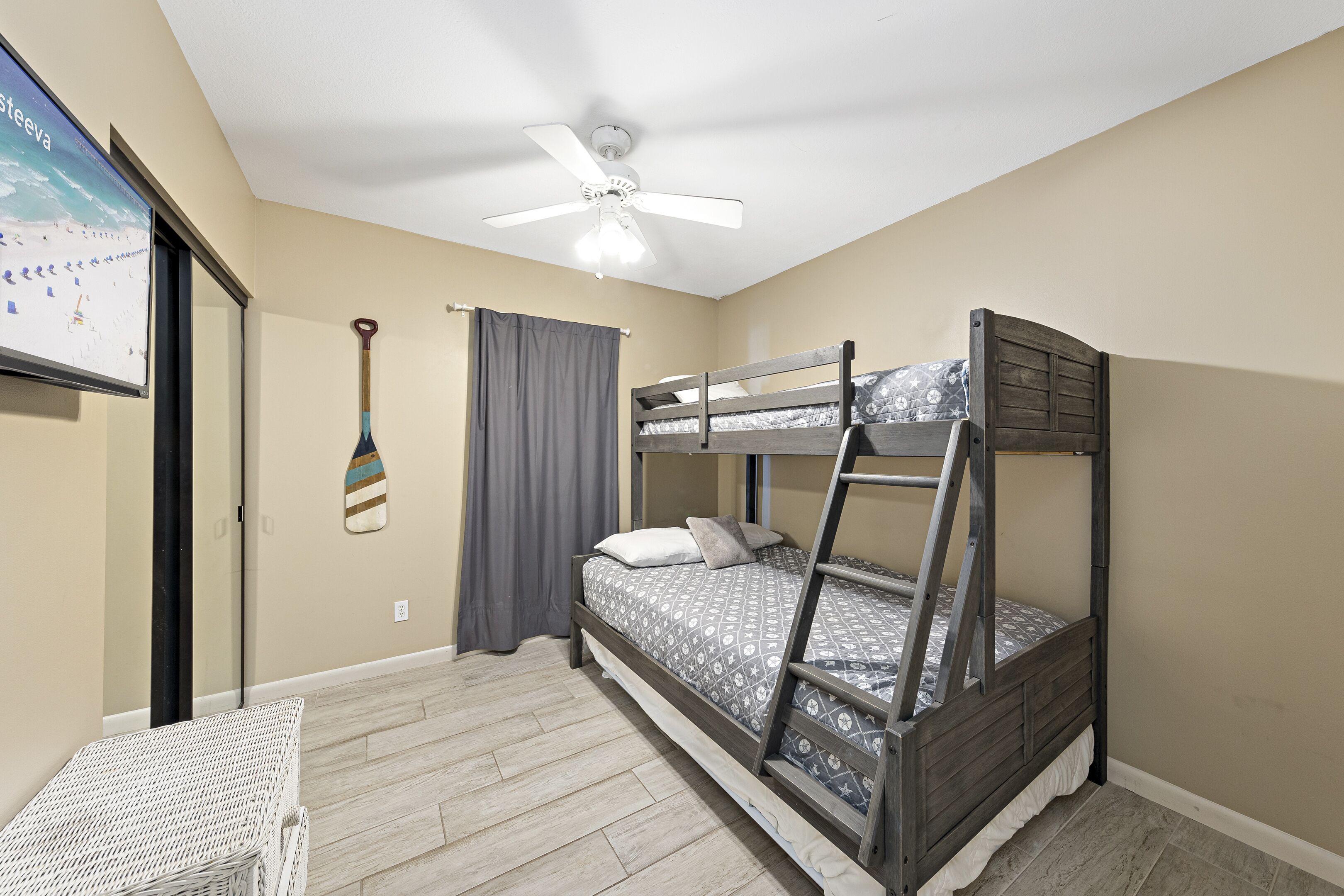 A bunk bed room with a ceiling fan, a small table, and a wall-mounted TV.