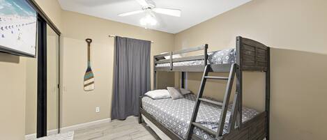 A bunk bed room with a ceiling fan, a small table, and a wall-mounted TV.