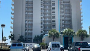 A multi-story hotel with a central vertical blue stripe, balconies on each floor, and palm trees in the foreground. - Shoalwater 804 (Orange Beach)