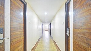 A long, narrow hallway with wooden doors on both sides and a tiled floor. - PPH Living Tricolours (Coimbatore)