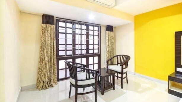 A room with a dining table and chairs, a window with a metal grid, and a yellow wall. - PPH Living Tricolours (Coimbatore)