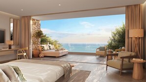 Une chambre moderne avec un grand lit, un canapé, un fauteuil et un bureau. Une grande fenêtre offre une vue sur l’océan.