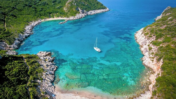 Une zone côtière aux eaux turquoise et limpides, avec un petit bateau, des rivages rocheux et de luxuriantes collines verdoyantes.