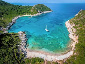 A coastal area with clear turquoise waters, a small boat, rocky shores, and lush green hills. - Ikos Odisia - All Inclusive (Corfu)