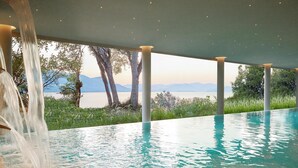 Une piscine agrémentée d’une cascade, entourée de colonnes et offrant une vue sur un lac et des montagnes.