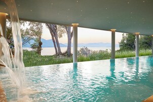 Une piscine agrémentée d’une cascade, entourée de colonnes et offrant une vue sur un lac et des montagnes.
