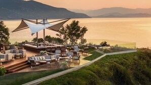 Une terrasse avec des sièges extérieurs, offrant une vue sur un plan d’eau paisible et des montagnes lointaines.