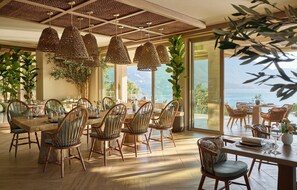 A dining area with wicker chairs, a wooden table, and hanging wicker lamps. - Ikos Odisia - All Inclusive (Corfu)