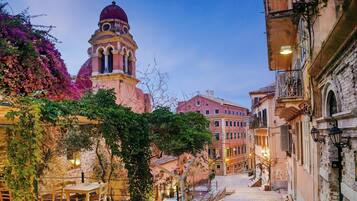 Una strada acciottolata fiancheggiata da edifici, con un campanile e tavolini e sedie all'aperto.