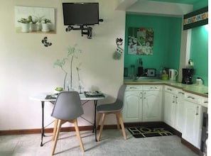Uma cozinha compacta com área de refeições, uma TV fixada na parede e uma parede de destaque verde.