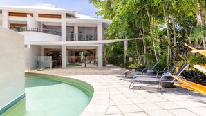 Een modern hotel met een zwembad, terras en weelderige tropische beplanting.