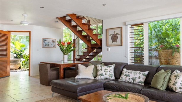 Een moderne woonkamer met een donker leren bank, een houten trap en een uitzicht op weelderig groen via grote ramen.
