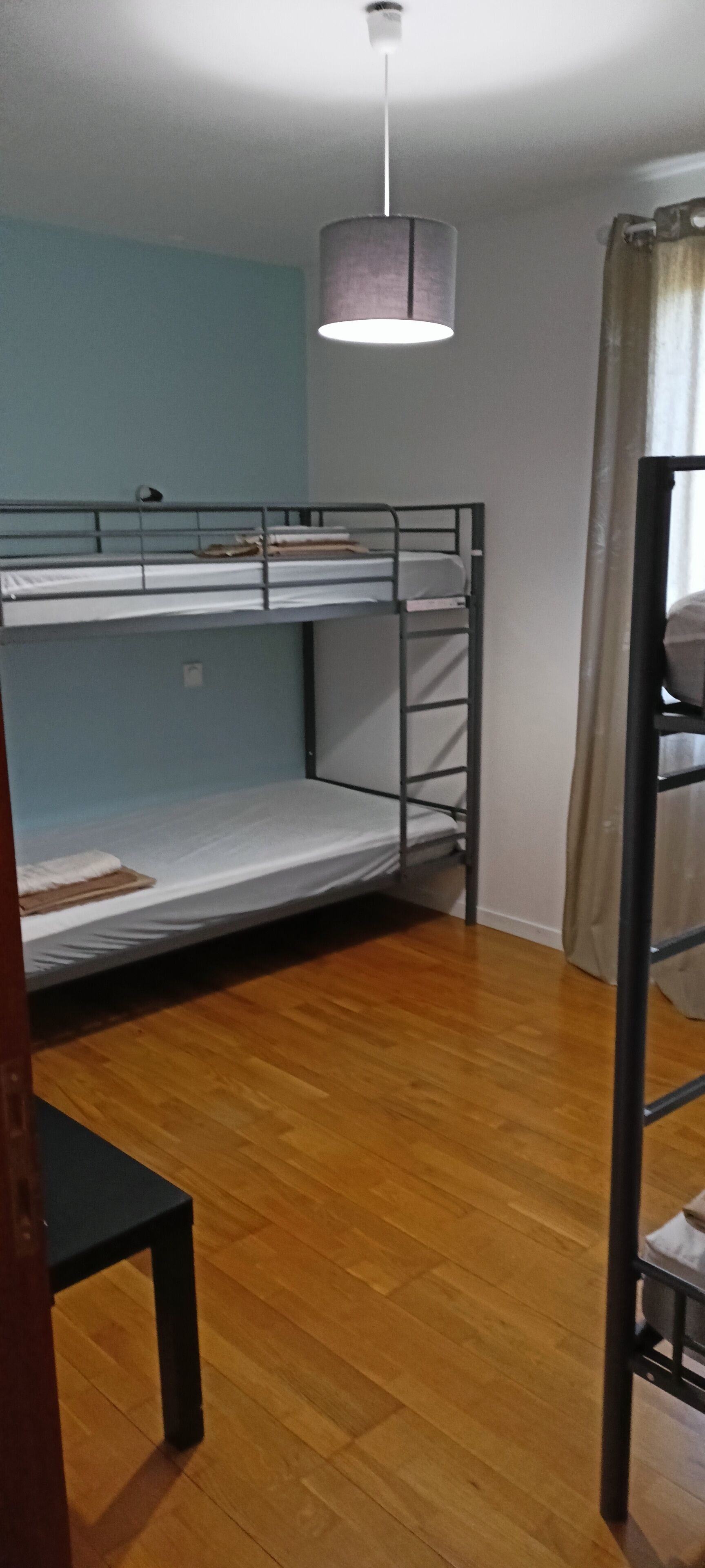 A room with bunk beds, a hanging light fixture, and a wooden floor.