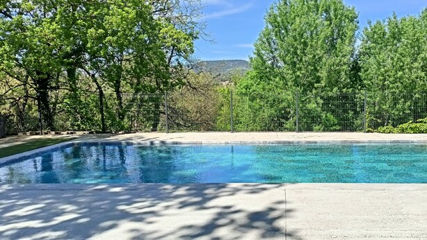 A rectangular swimming pool with clear blue water, surrounded by a concrete deck and a metal fence. - Gîte en Pleine Nature (Valaurie)