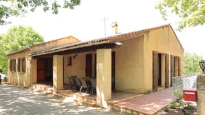 A single-story building with a tiled roof, a porch with chairs, and a small garden area. - Gîte en Pleine Nature (Valaurie)