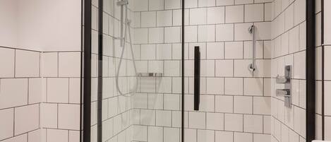 A modern bathroom with a glass-enclosed shower, white tiled walls, a toilet, and a towel on the floor.