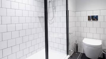 Un baño moderno con paredes de azulejos blancos, mampara de ducha de vidrio, inodoro blanco y suelo negro.