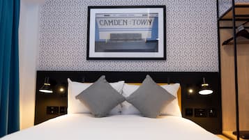 Quarto de hotel moderno com uma moldura exibindo uma imagem de Camden Town, uma cama bem arrumada com duas almofadas, luminárias laterais e uma cabeceira de madeira.