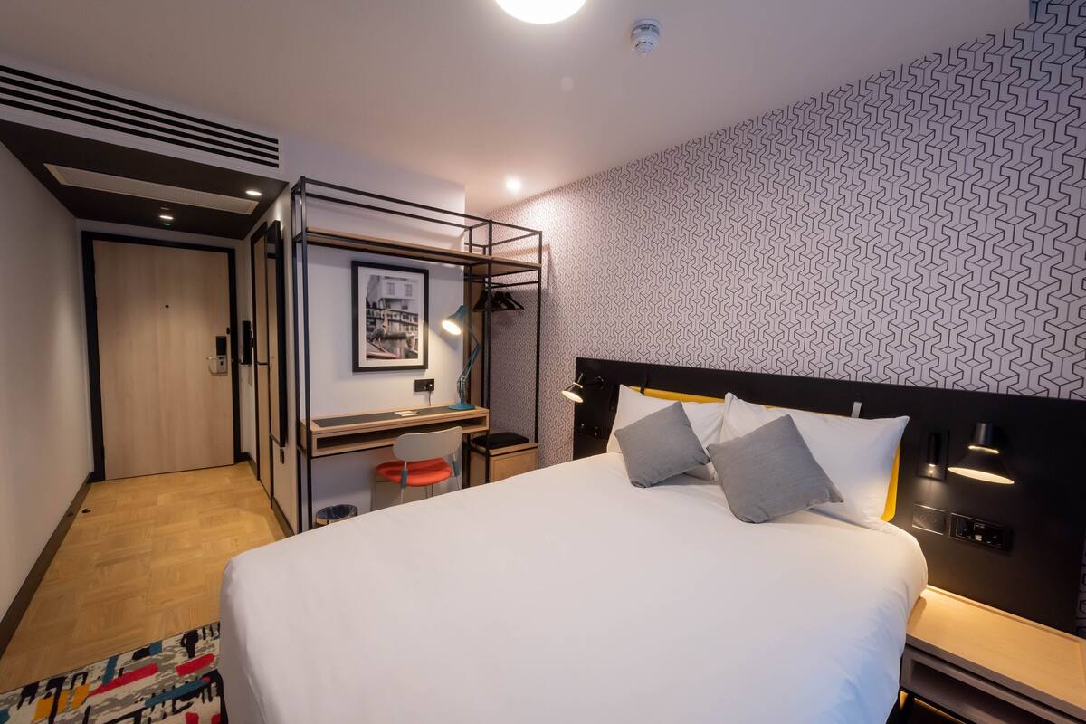 A modern hotel room with a large bed, a desk, and a chair.