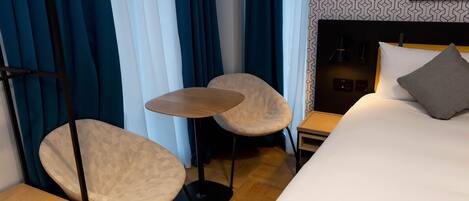 Ein Hotelzimmer mit einem Bett, zwei Stühlen, einem kleinen Tisch, einem Nachttisch und einer Wandlampe.
