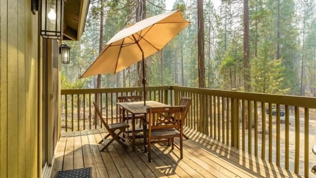 Una terraza de madera con una mesa, sillas y una sombrilla, con vistas a un bosque.