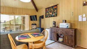 Interior acogedor de una cabaña con una mesa de comedor de madera, sillas, un sofá, chimenea, televisor y un cuadro en la pared.