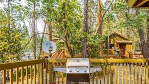 Una terraza con una parrilla, rodeada por un cerco de madera y árboles.