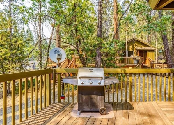 A deck with a barbecue grill, surrounded by a wooden fence and trees.