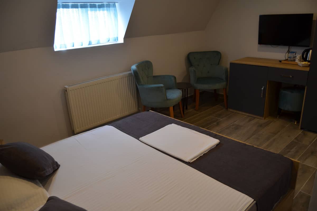 A room with a bed, two chairs, a desk, and a TV.