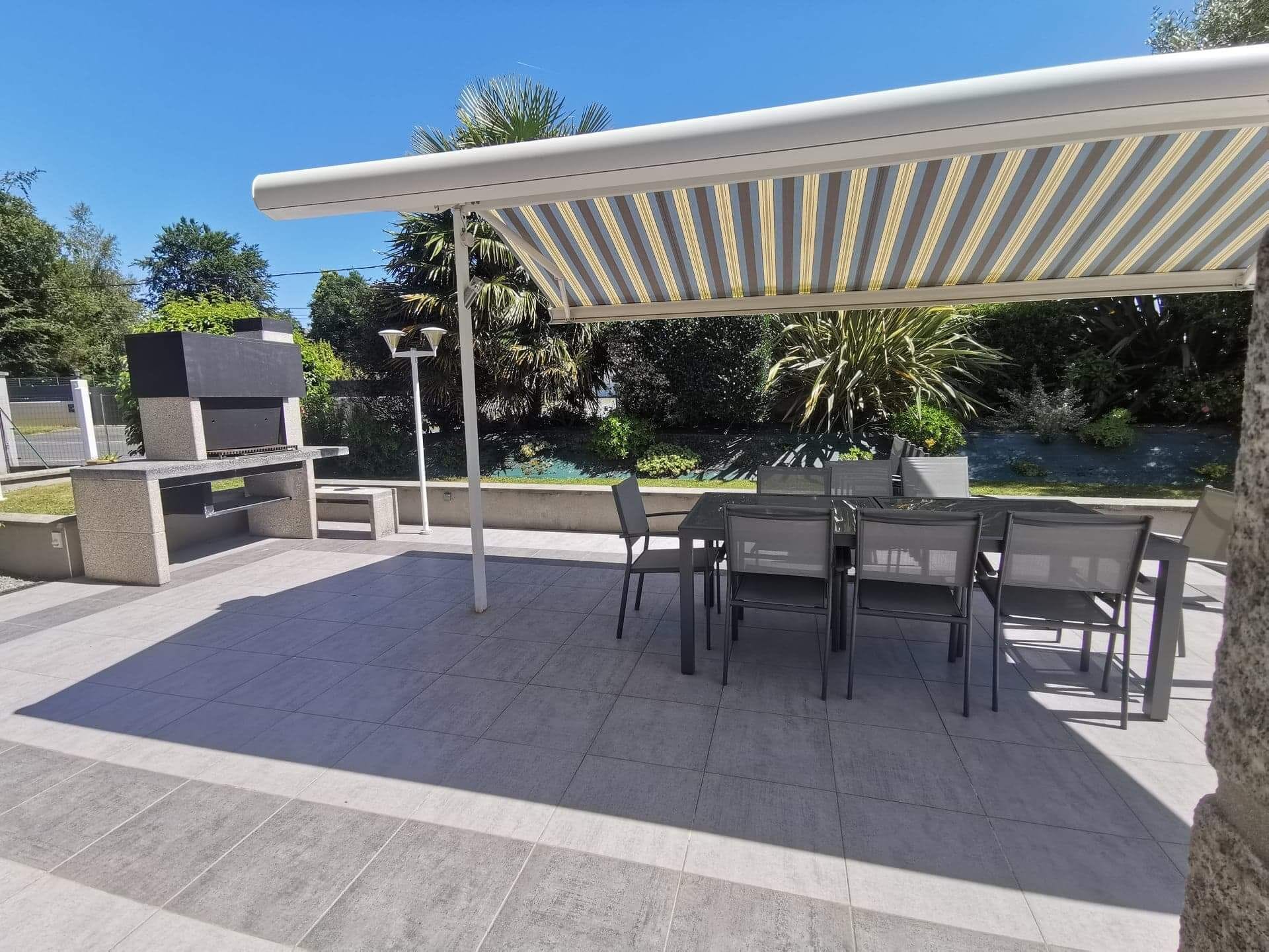 Eine Terrasse im Freien mit Grill, Sitzgelegenheit und einem Pool im Hintergrund.