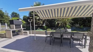 An outdoor patio with a grill, seating area, and a pool in the background. - Loft Proche Plage (Pleslin-Trigavou)